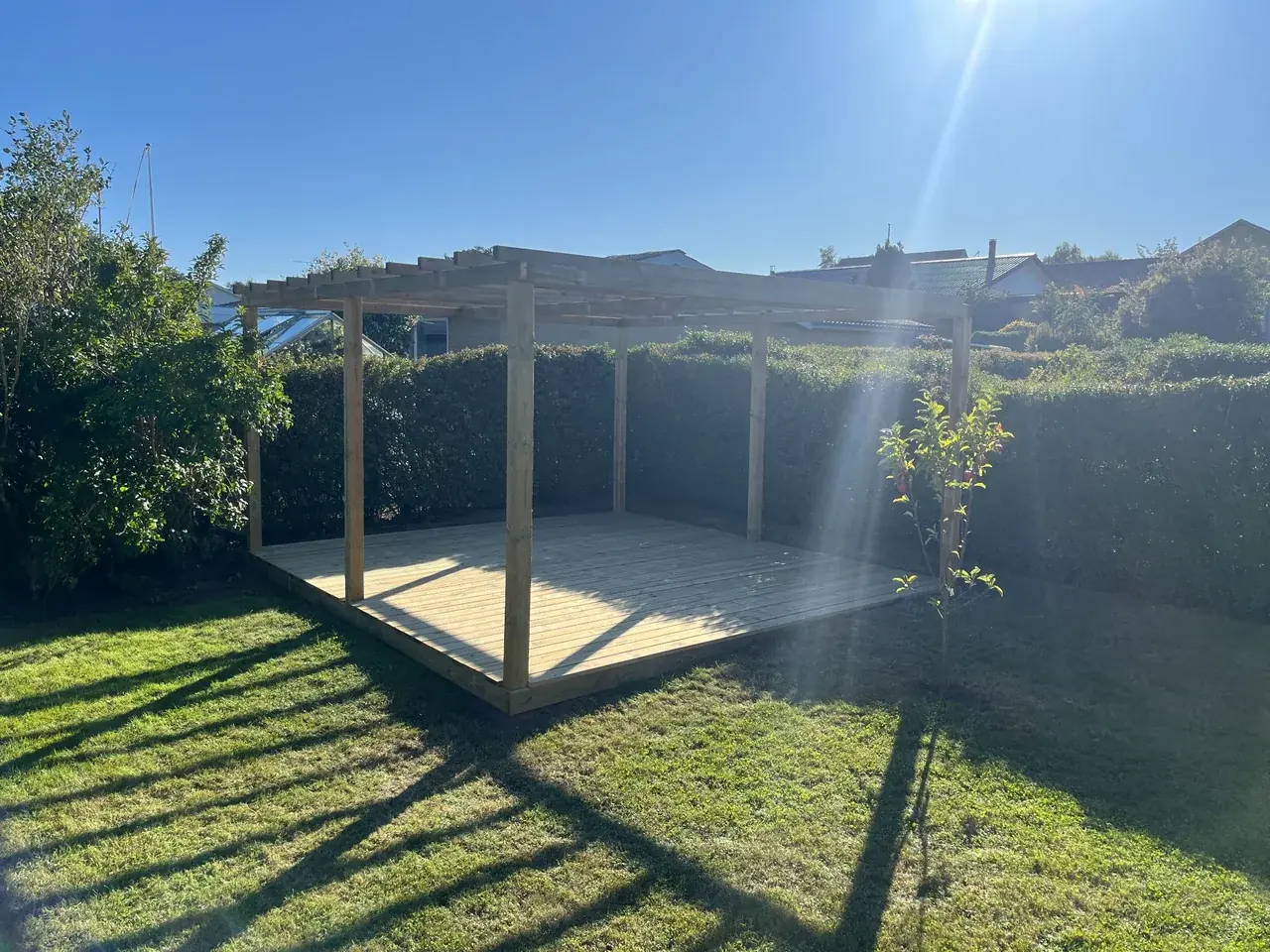 Færdig træterrasse med pergola omgivet af hæk